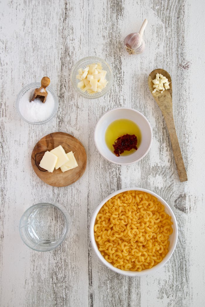 services-01 Overhead view of macaroni and ingredients including cheese, garlic, and spices on a rustic table.