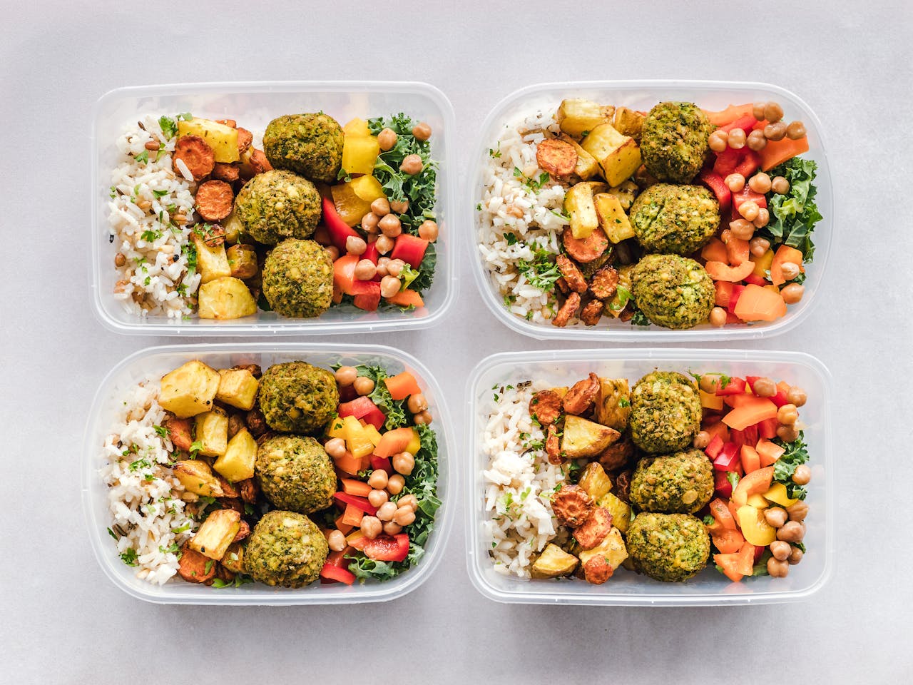 services-03 Colorful meal prep containers with falafel, chickpeas, rice, and vegetables for a healthy lifestyle.